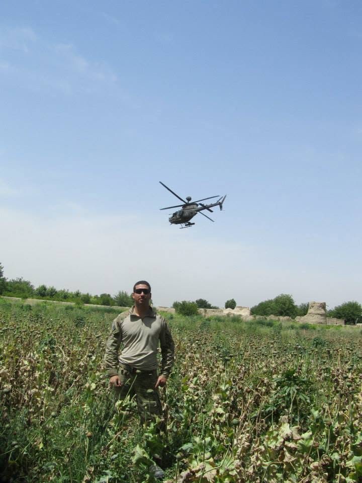 Josh Goldberg standing in a field in Kandahar, Afghanistan, in 2012, with a helicopter overhead