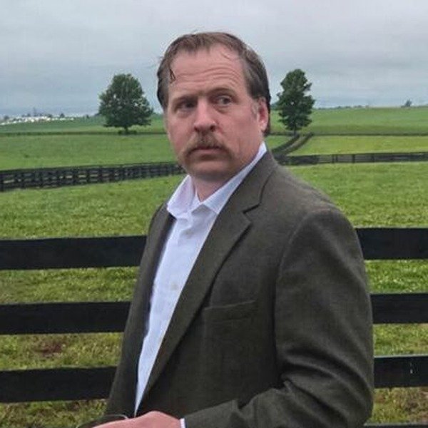 Patrick Colton in a jacket and open collar at a pasture fence, summer 2026